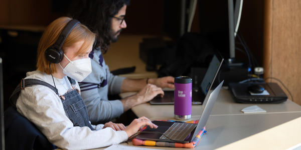 two students sit working on laptops together