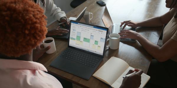 three people use laptops, one laptop screen shows a calendar