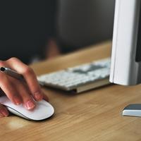 hand on a mouse holding a pen next to a computer and keyboard