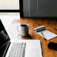 macbook with coffee and notepad and phone on a wooden table