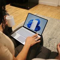 overhead photo of a person typing on a windows 11 laptop and holding coffee mug